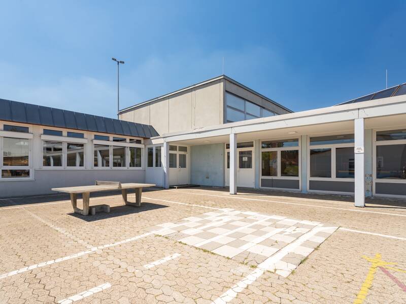 Das Bild zeigt den Schulhof mit einer Tischtennisplatte unter einem blauen Himmel.
