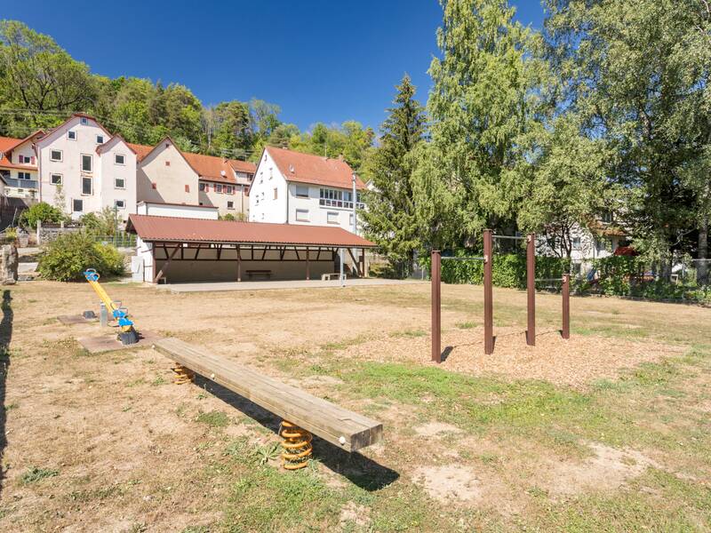 Das Bild zeigt den Schulhof mit Spielgeräten unter einem blauen Himmel.