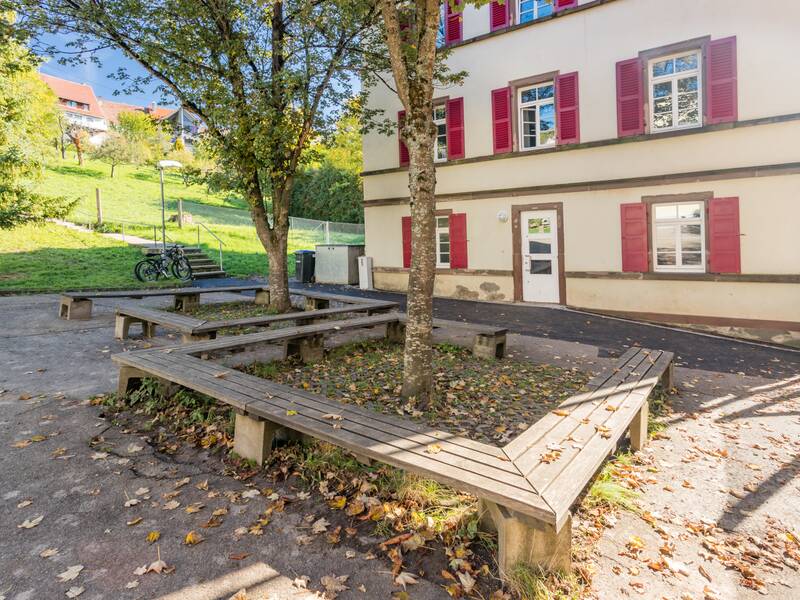 Ein Schulhof mit Sitzgelegenheiten und dem Schuleingang.