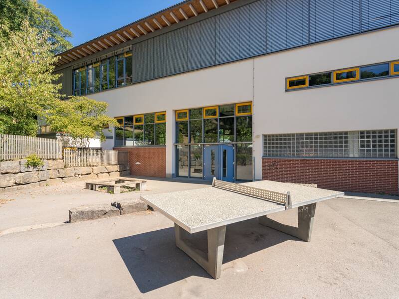 Ein Schulhof mit einer Tischtennisplatte und dem Schuleingang.