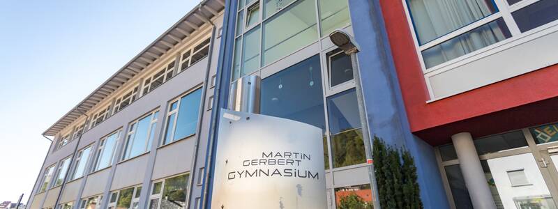 Ein modernes Schulgebäude mit großen Fenstern und einem Schild mit der Aufschrift "Martin Gerbert Gymnasium" ist zu sehen.