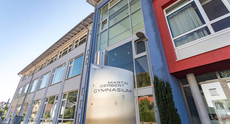Ein modernes Schulgebäude mit großen Fenstern und einem Schild mit der Aufschrift "Martin Gerbert Gymnasium" ist zu sehen.