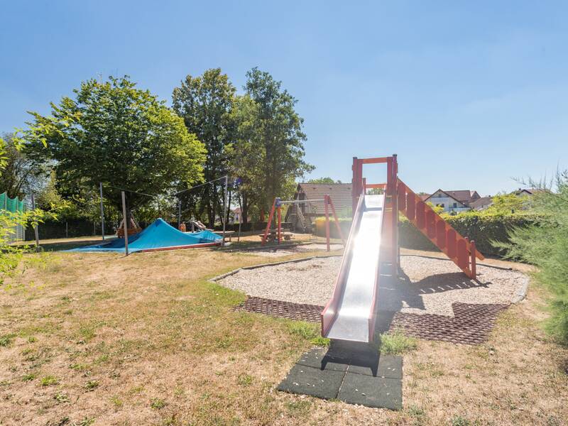 Das Bild zeigt den Schulhof unter einem Blauen Himmel mit einer Rutsche.