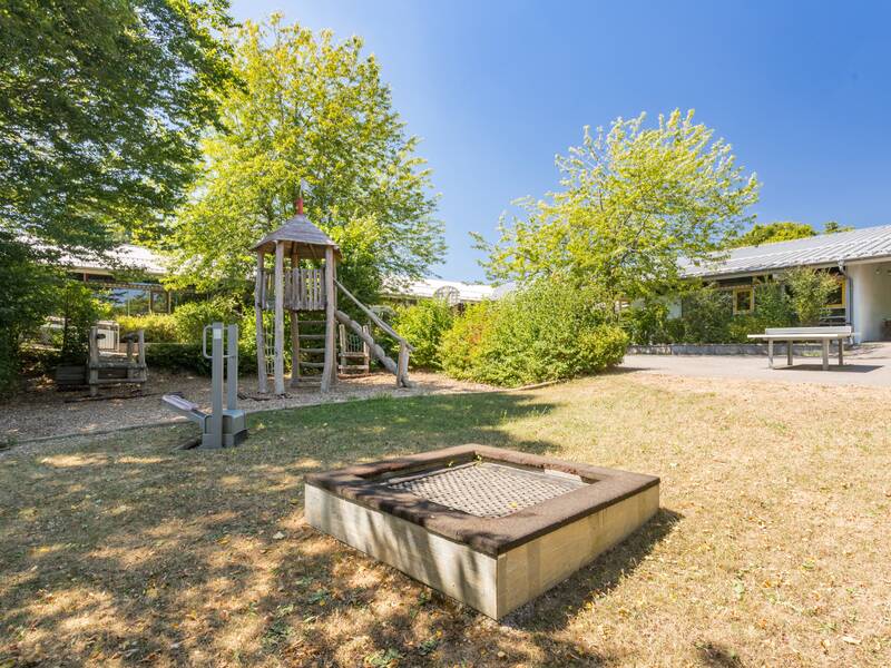Das Bild zeigt den Schulhof mit Spielgeräten unter einem blauen Himmel.