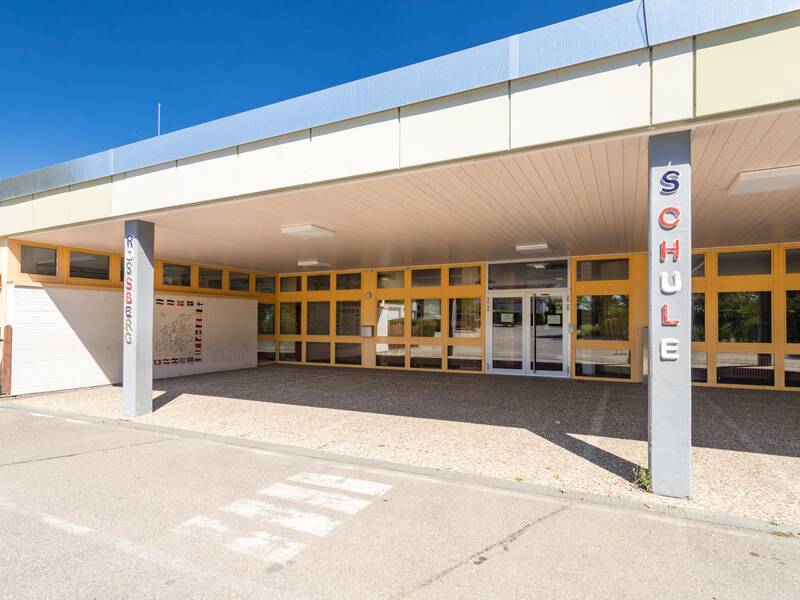 Ein überdachter Schuleingang unter blauen Himmel.