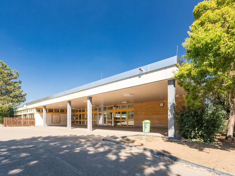 Ein überdachter Schuleingang unter blauen Himmel.