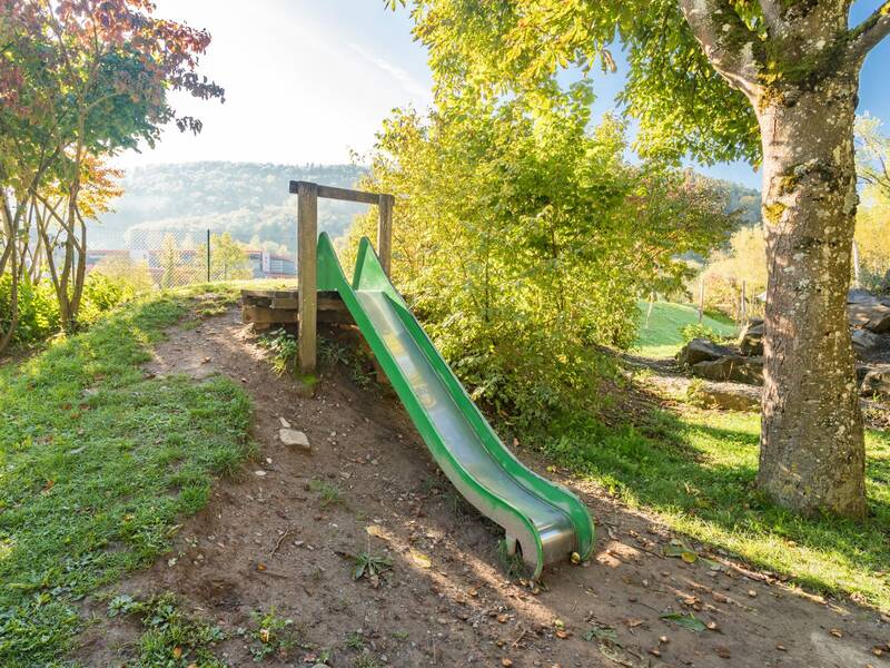grüne Metallrutsche an einem Hang umgeben von Bäumen