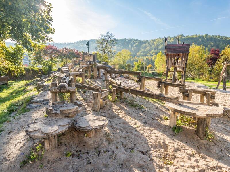 ein Spielplatz mit Sandkasten und Holzkonstruktionen als Wasserlauf
