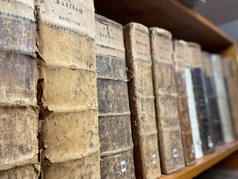 Reihe alter, abgenutzter Bücher mit braunen und schwarzen Einbänden auf einem Regal.