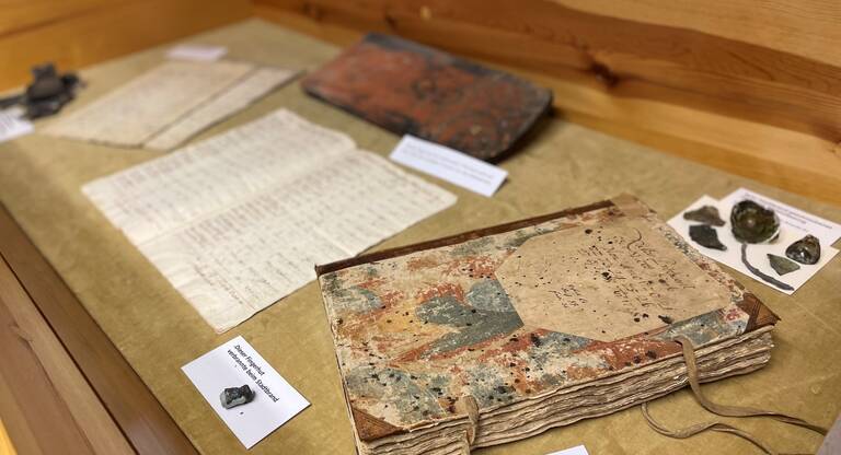 Alte, vergilbte Dokumente und ein gebundenes Buch mit handgeschriebenen Texten in einer Museumsvitrine
