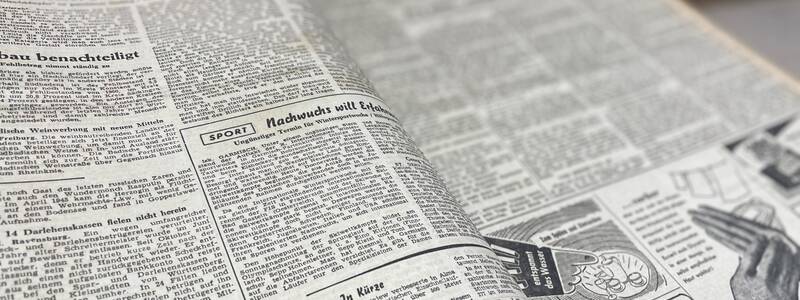 Nahaufnahme einer aufgeschlagenen Zeitung mit Textartikeln und einer Anzeige für 'Stehmarke'.