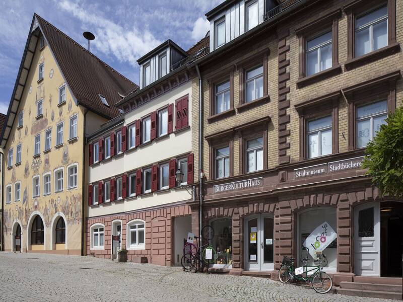 Eine Straße mit historischen Gebäuden, darunter ein Bürgerkulturhaus und ein bemaltes Gebäude mit vielen Fenstern.