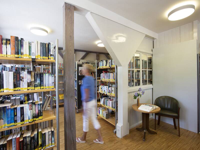 Eine Person geht an Regalen voller Bücher in einer gut beleuchteten Bücherei vorbei.