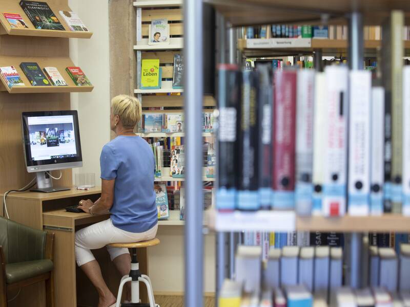 Eine Person, die vor dem Bildschirm sitzt, umgeben von Bücherregalen