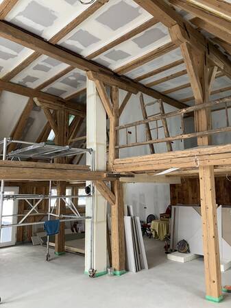 Eine Baustelle in einem Gebäude mit freiliegenden Holzbalken und einem Gerüst im Vordergrund.