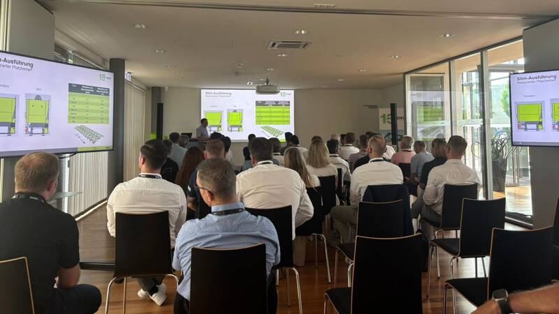 Ein Konferenzraum mit mehreren Personen, die in Richtung eines Präsentationsbildschirms sitzen, auf dem technische Diagramme zu sehen sind.