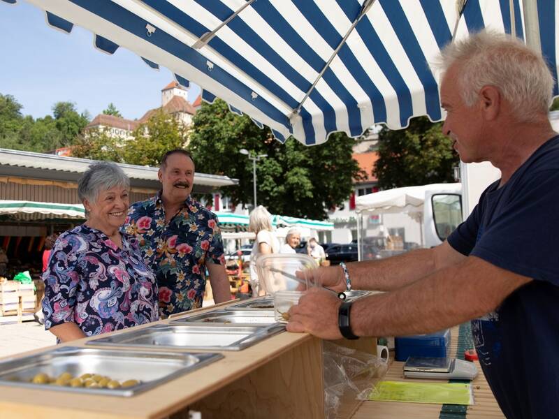 Ein Mann verkauft an einem Stand etwas an zwei Personen.