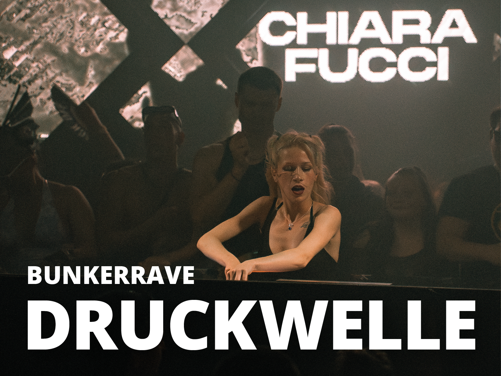 Eine Person steht hinter einem DJ-Pult in einem dunklen Raum mit der Aufschrift "Chiara Fucci" und "Bunkerrave Druckwelle" auf der oberen und unteren Bildhälfte.